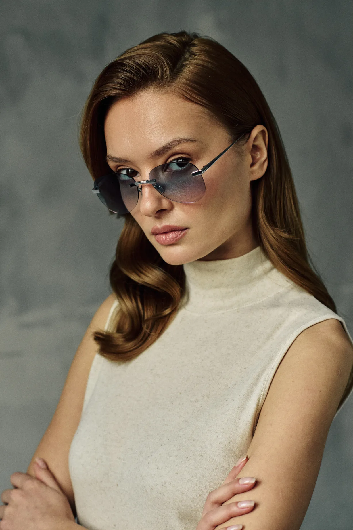 Woman in a cream sleeveless turtleneck wearing PTERON Azure silver aviator sunglasses with blue gradient lenses