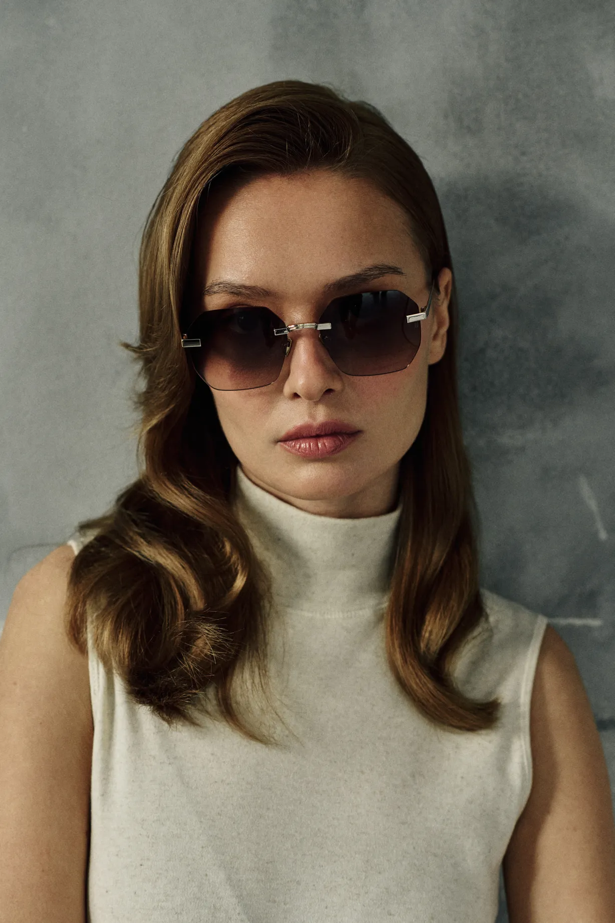Woman in a cream sleeveless turtleneck wearing IRIS Bronze rimless hexagonal titanium sunglasses
