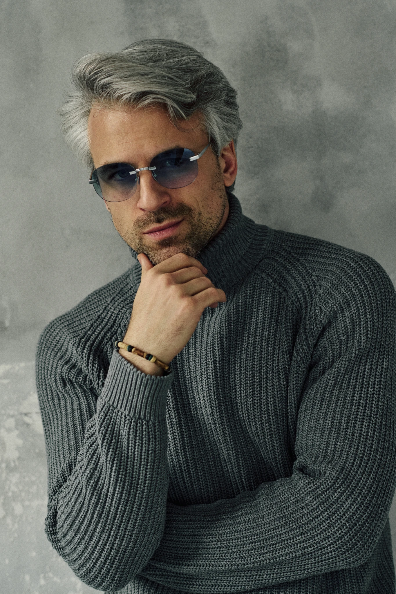 Man in a grey knit turtleneck wearing KAIROS Crystal silver oval sunglasses with blue gradient lenses