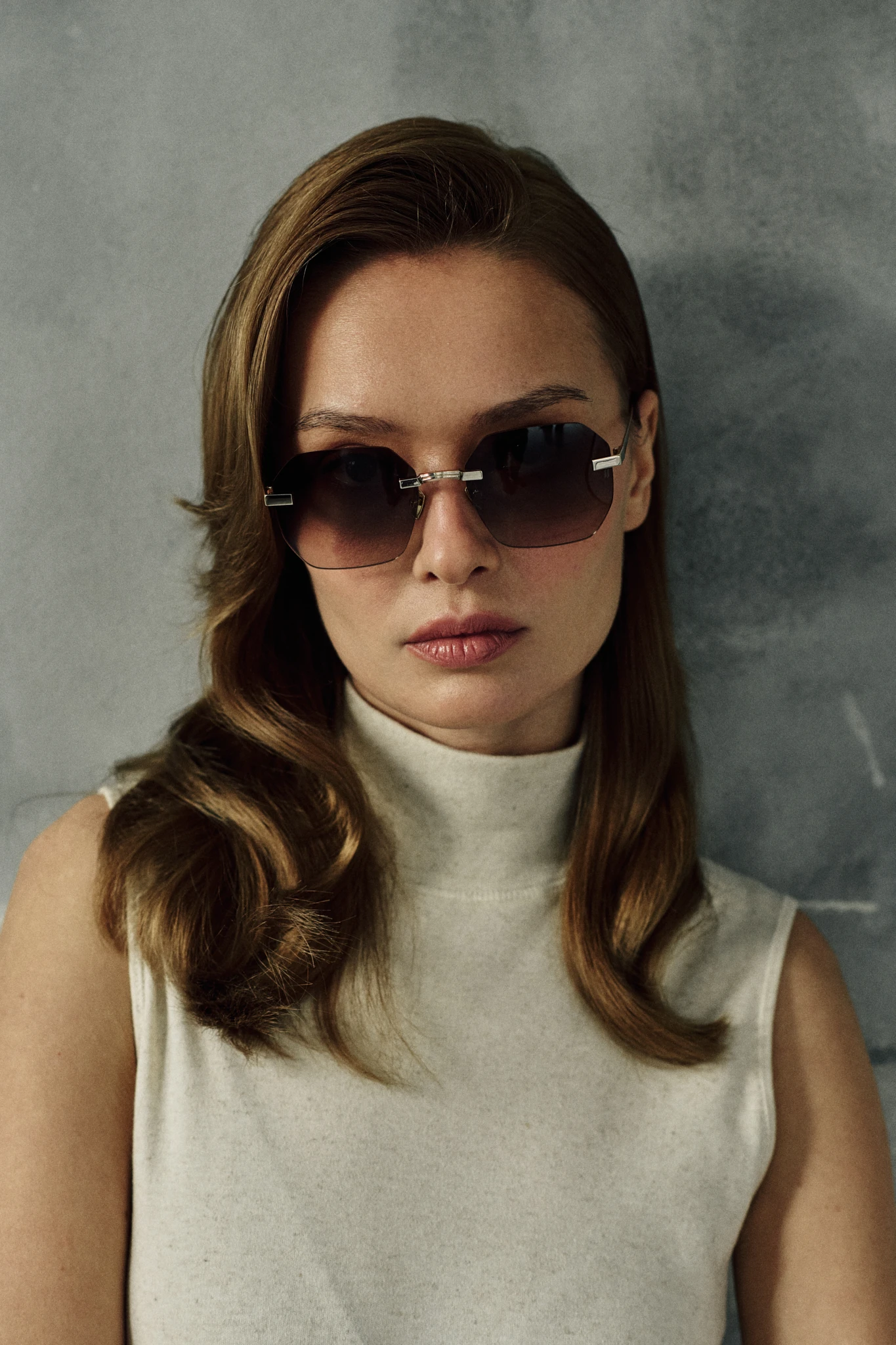 Woman in a cream sleeveless turtleneck wearing IRIS Bronze rimless hexagonal titanium sunglasses
