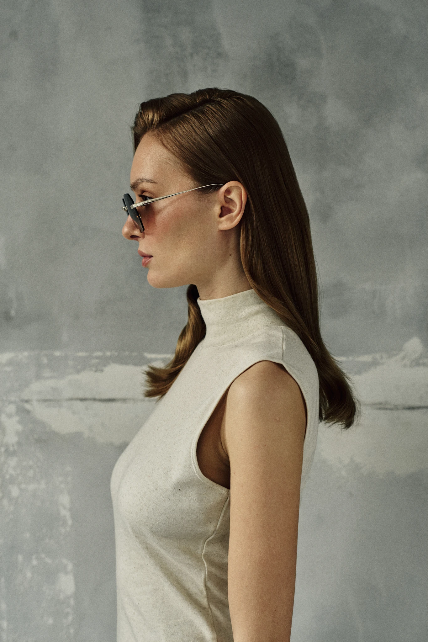 Side profile of a woman in a cream sleeveless turtleneck wearing IRIS Moss gold titanium sunglasses with green gradient lenses