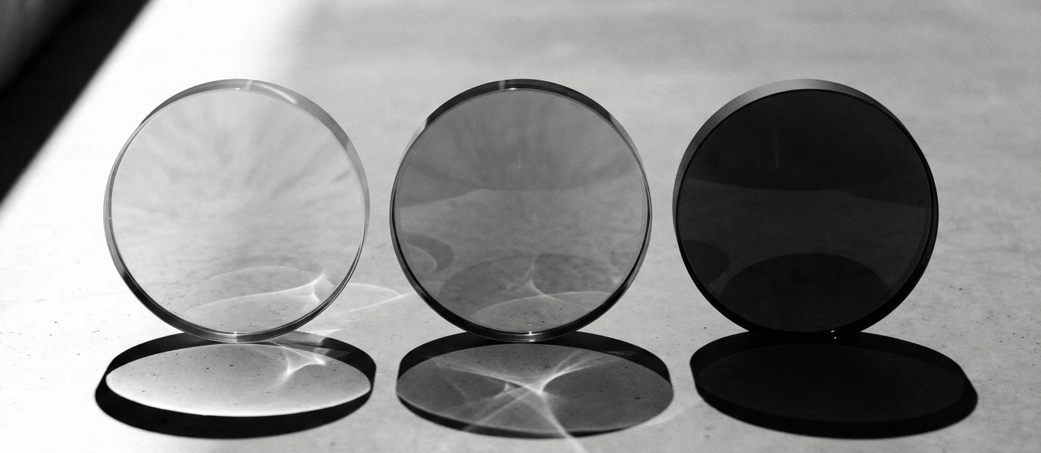 Three lenses on a sunlit surface, from clear to almost black