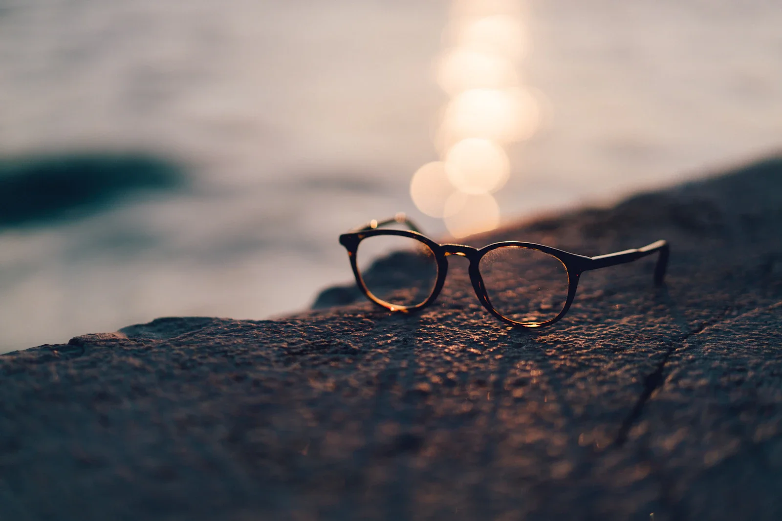 Close-up of sunglasses lens reflecting sunlight near water, illustrating tint and glare reduction